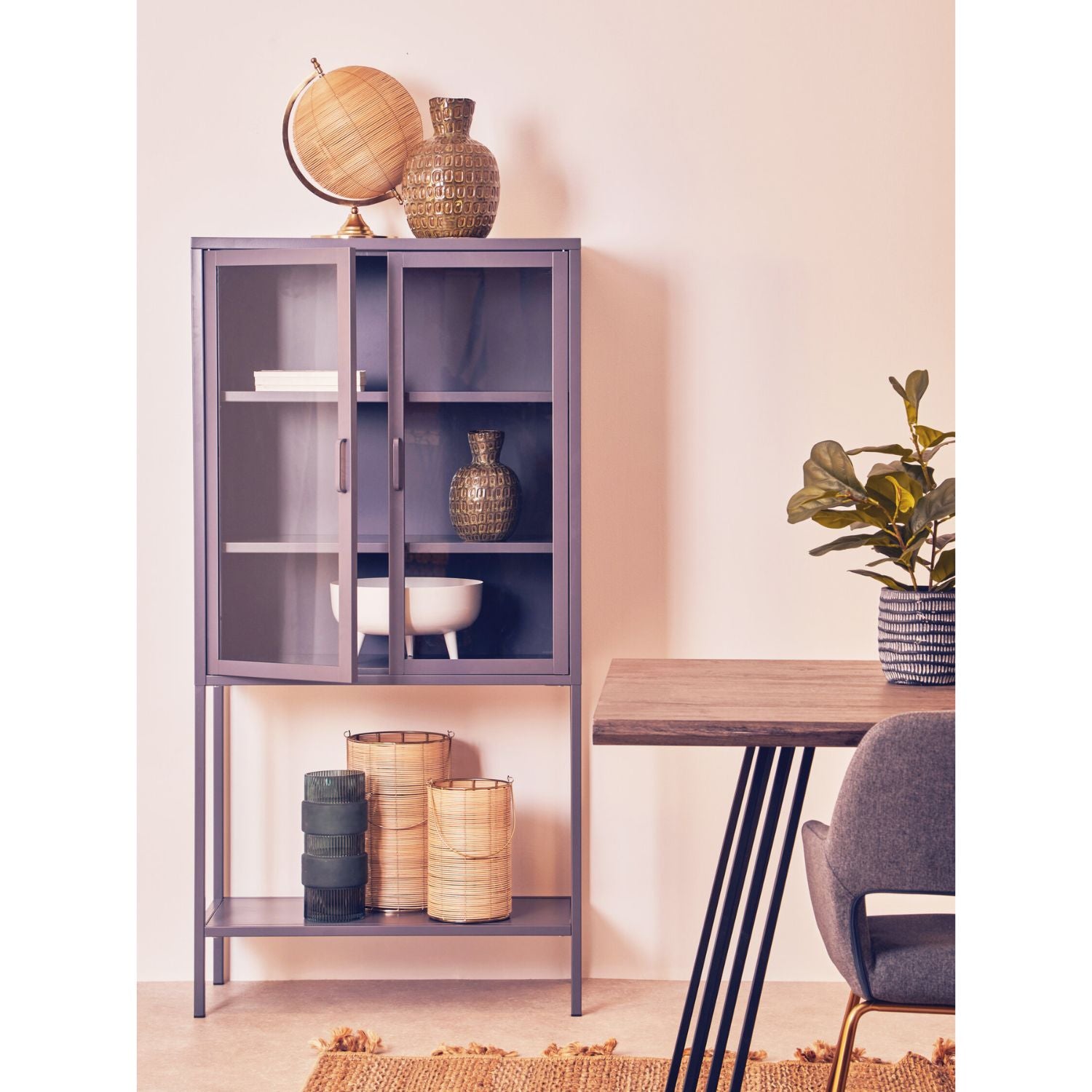 Purple glass-fronted cabinet with decorative items in a room with a wooden table and plant.