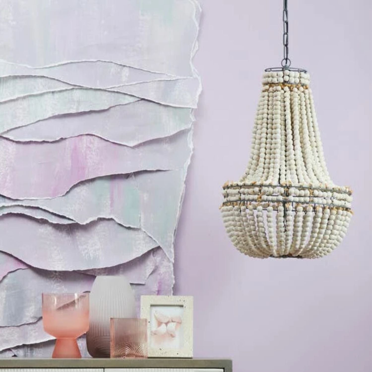 Decorative chandelier hanging above a shelf with decorative items against a light purple wall.