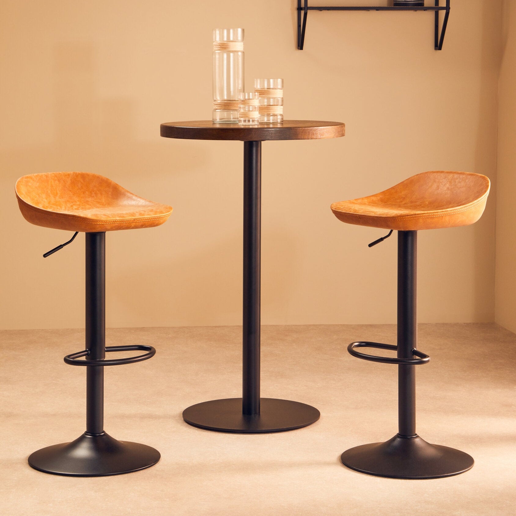 Two wooden bar stools with black metal legs in front of a small round table against a beige wall.