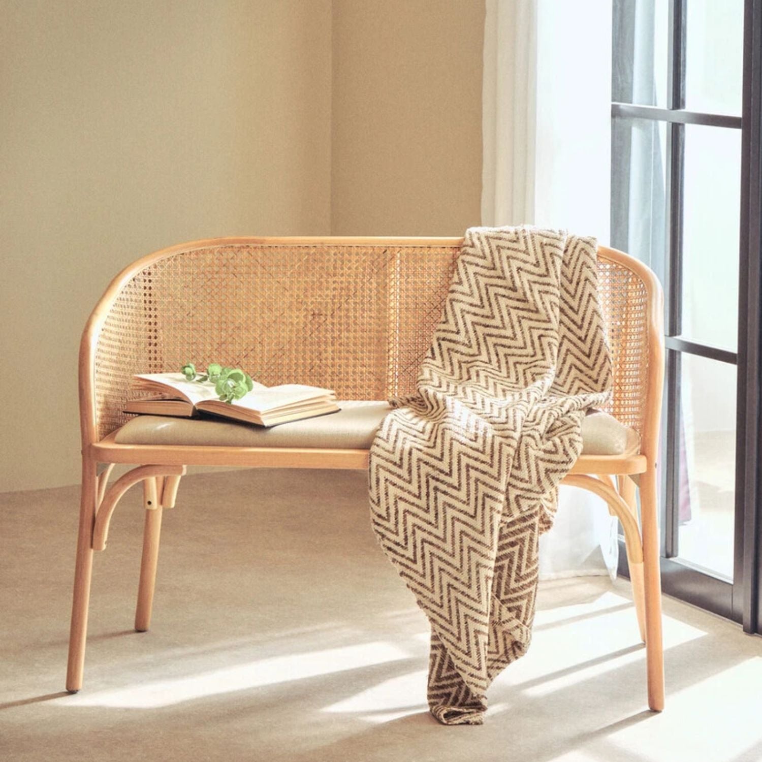 Wicker bench with a patterned throw blanket and open book in a bright room.