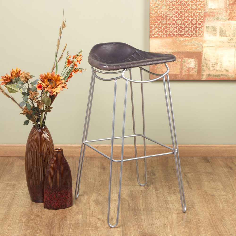Bar stool with metal legs and leather seat next to a vase of flowers on a wooden floor.