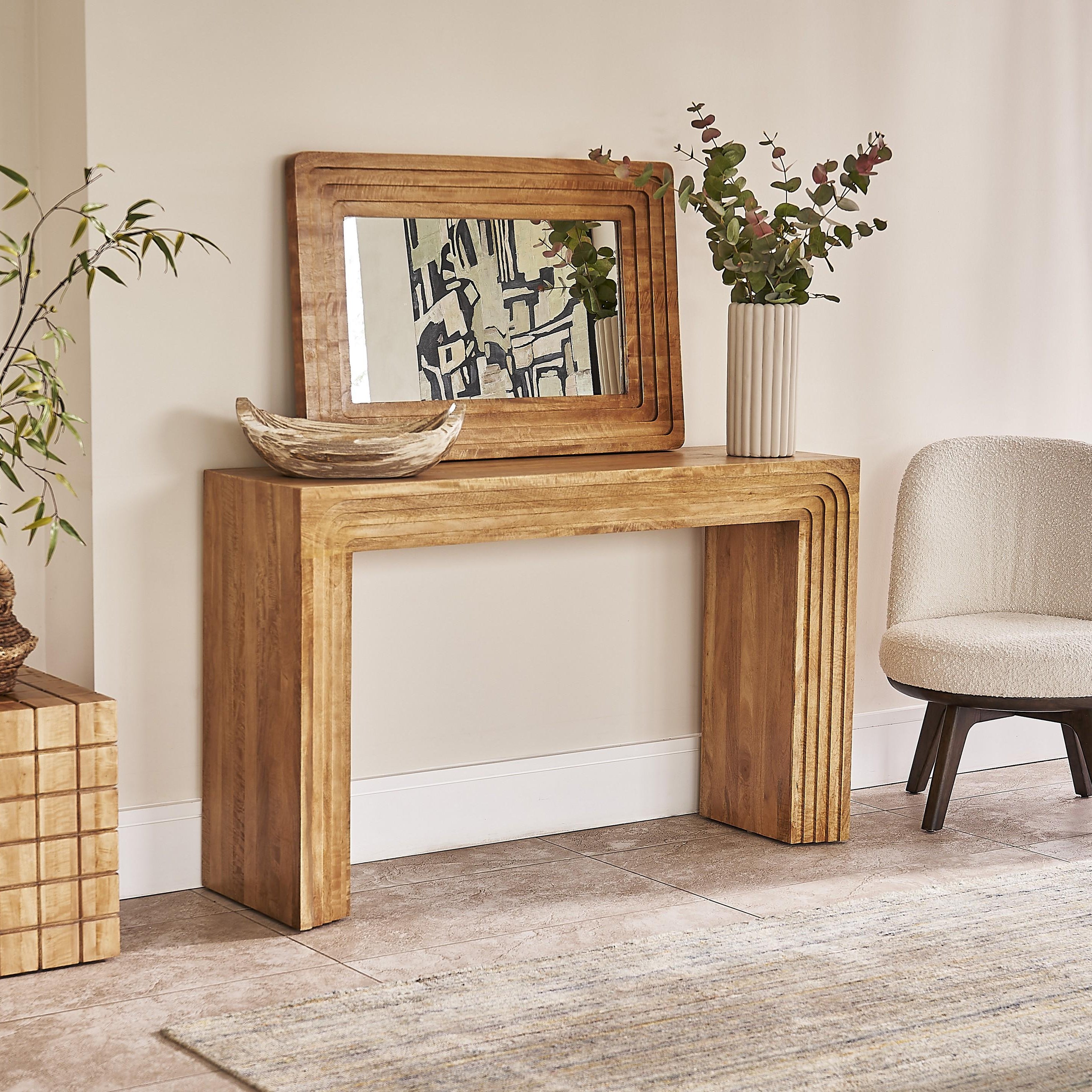 Wooden console table with mirror, decorative items, and a chair in a room.