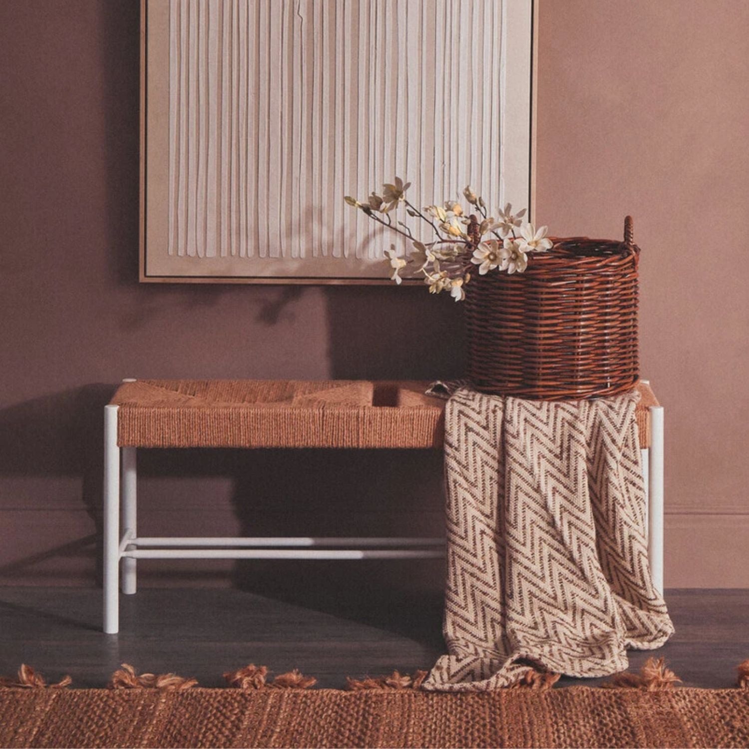 Wicker bench with a woven basket and blanket against a brown wall.