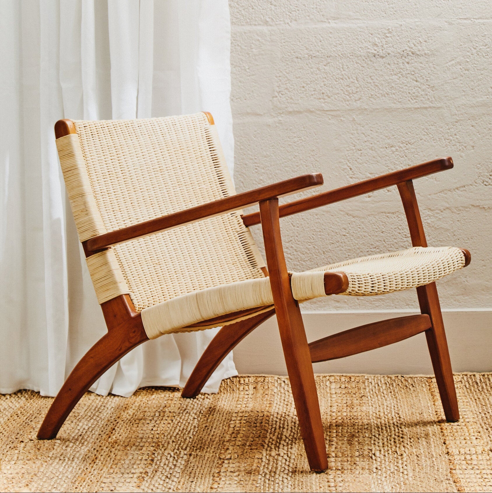Wooden chair with woven seat and backrest in a room with white curtains and textured wall.