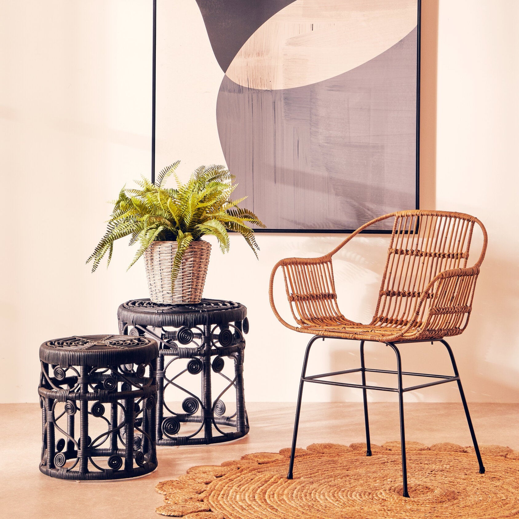 Wicker chair and side tables with a plant against a wall with abstract art