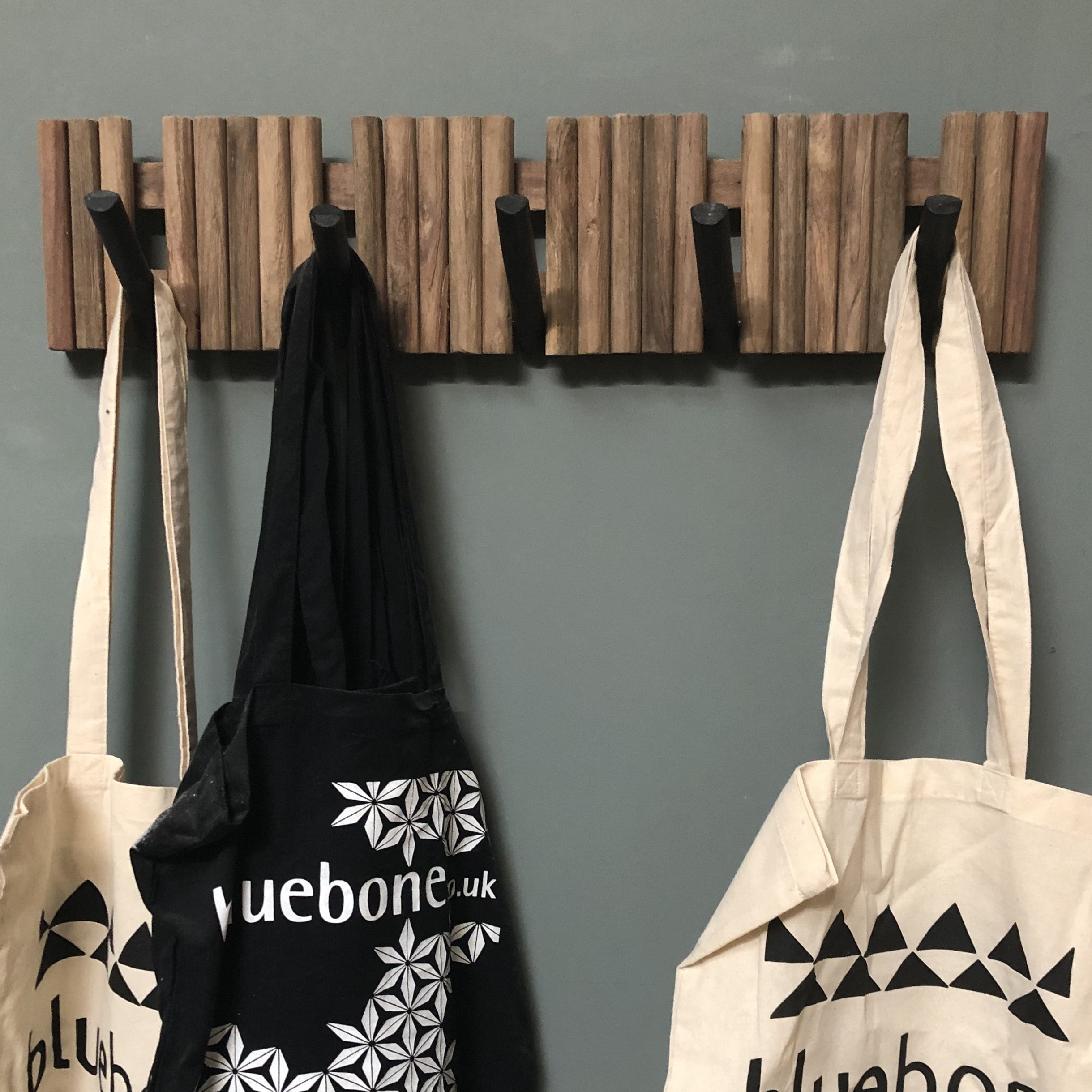 Tote bags with 'bluebone' branding hanging on a wooden hook rack against a gray wall.
