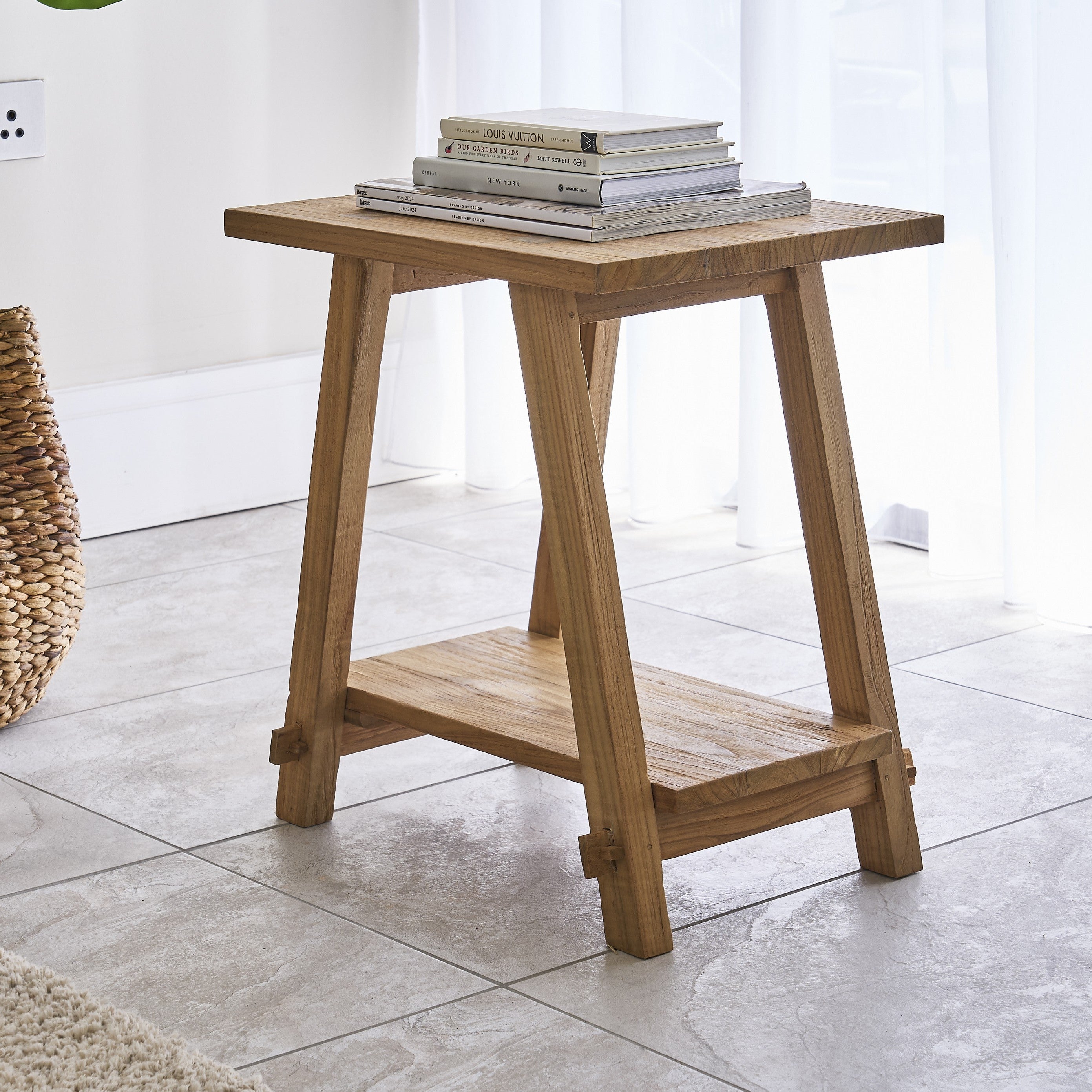 Wooden side table with books on a tiled floor in a bright room.