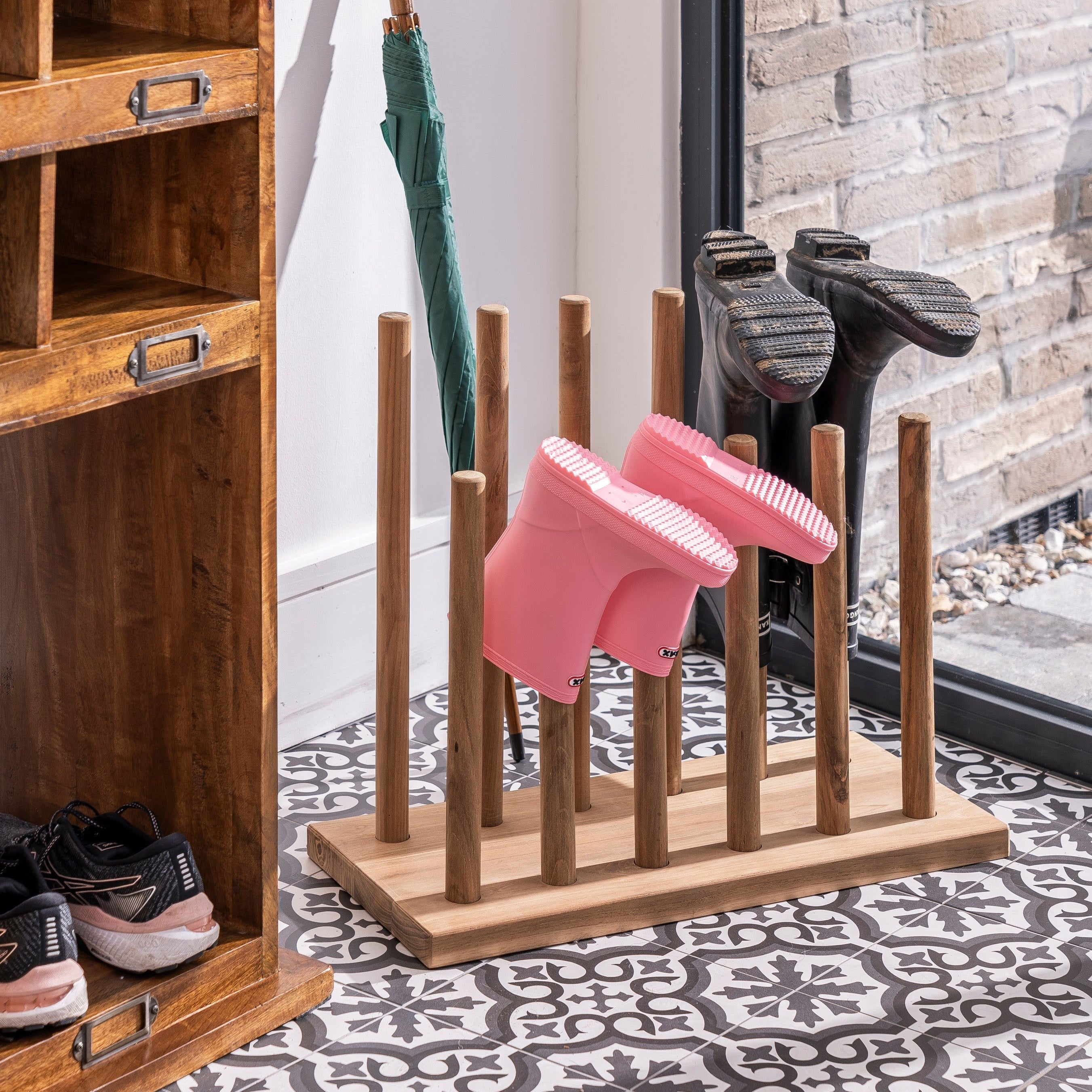 Wooden umbrella stand with a pink dog brush and green umbrella in a home setting.