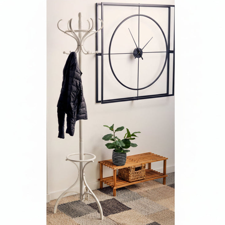 White coat rack with a black coat against a white wall with a clock, plant, and wooden side table.